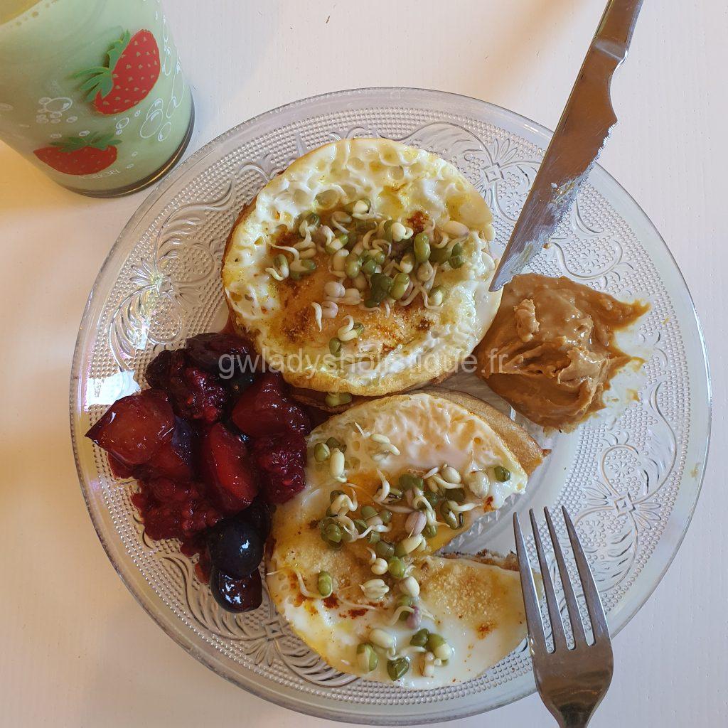 Petit-déjeuner équilibré avec oeufs, pancakes, graines germées, purée de cacahuètes et fruits frais.
